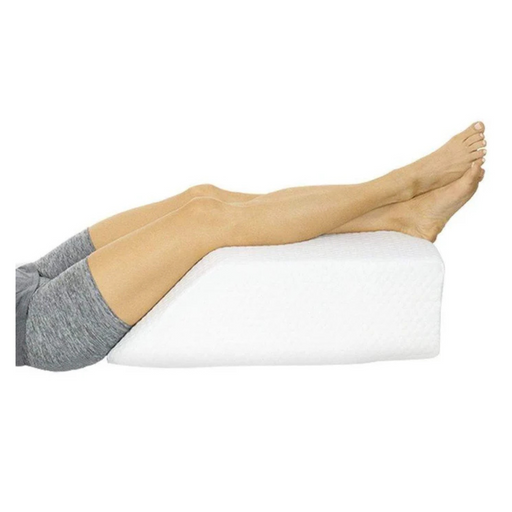 A person is comfortably lying on their back with legs elevated using the Vive Health Leg Rest Pillow, crafted for leg support. They wear gray shorts, enjoying the gel-infused memory foam designed for optimal relaxation and relief.