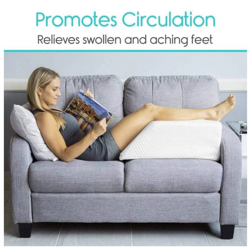 A woman lounges on a gray couch, using a Vive Health Leg Rest Pillow to elevate her legs while reading a magazine. The text above says Promotes Circulation and Relieves Swollen and Aching Feet.