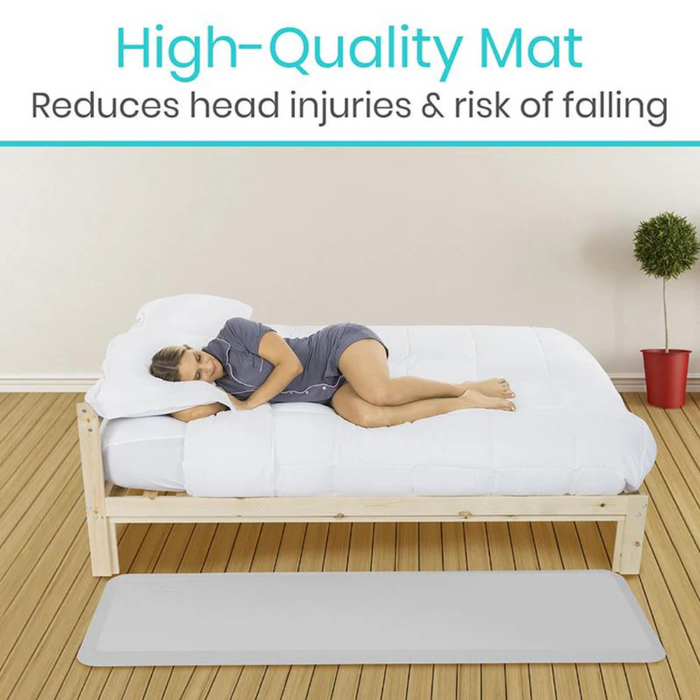 A woman sleeps on a bed with a thick comforter. Beneath, the Vive Health XL Bedside Padded Fall Mat rests on the wooden floor, designed to reduce head injuries & risk of falling with its impact-absorbing foam. A potted plant enhances the serene setting.