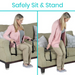 A woman, in a pink cardigan, grey top, and beige pants, uses the Vive Health Couch Stand Assist with an adjustable aluminum frame on a beige couch with patterned pillows. The text above reads Safely Sit & Stand.