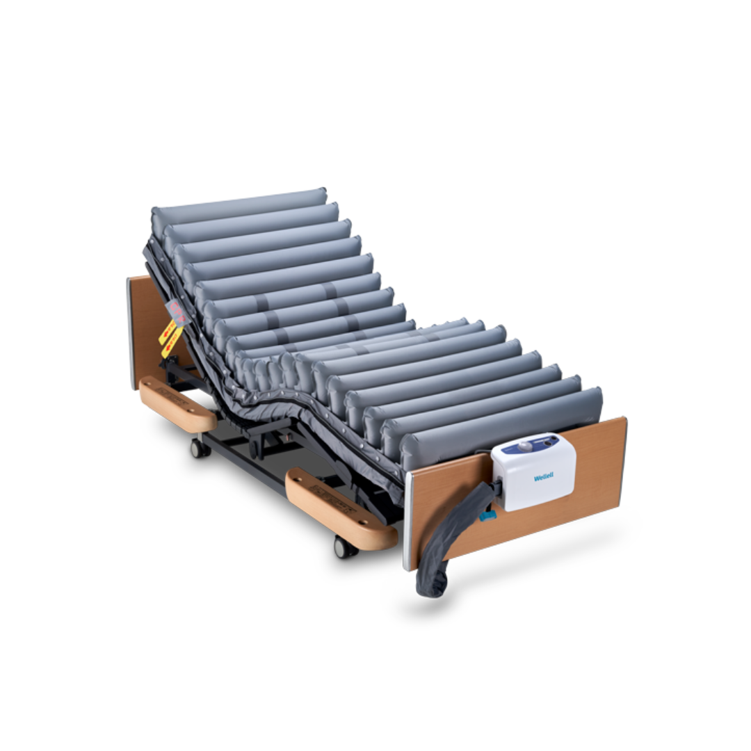 The Wellell Domus 3 Bariatric Alternating Pressure Mattress with Micro Low Air Loss is an adjustable medical bed featuring gray inflatable tubes, wood-panel head/foot boards, a foot control unit, and wheels. Ideal for long-term care and pressure redistribution.