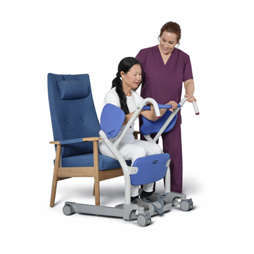 A woman uses the ARJO Sara Stedy Manual Standing Aid & Sit-To-Stand Transfer Lift to push a chair with the assistance of a walker.